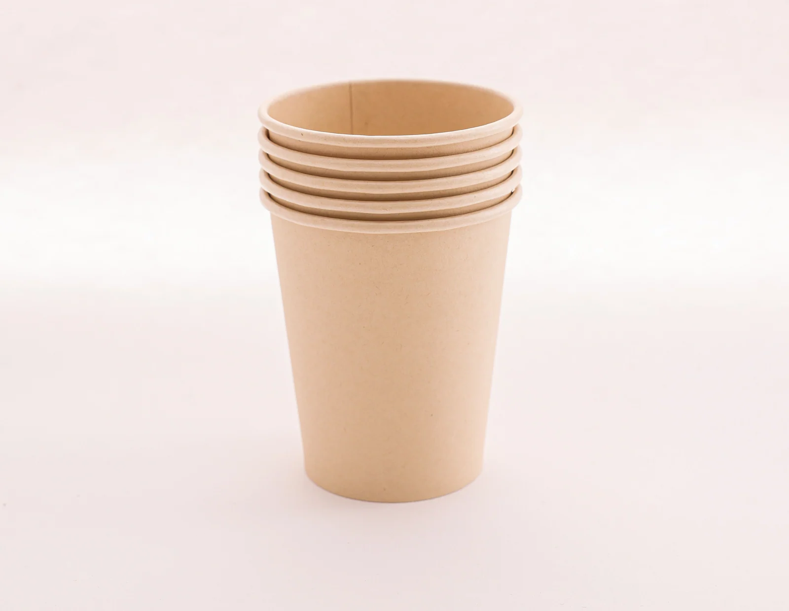 A stack of unprinted kraft paper cups on a warm ivory surface